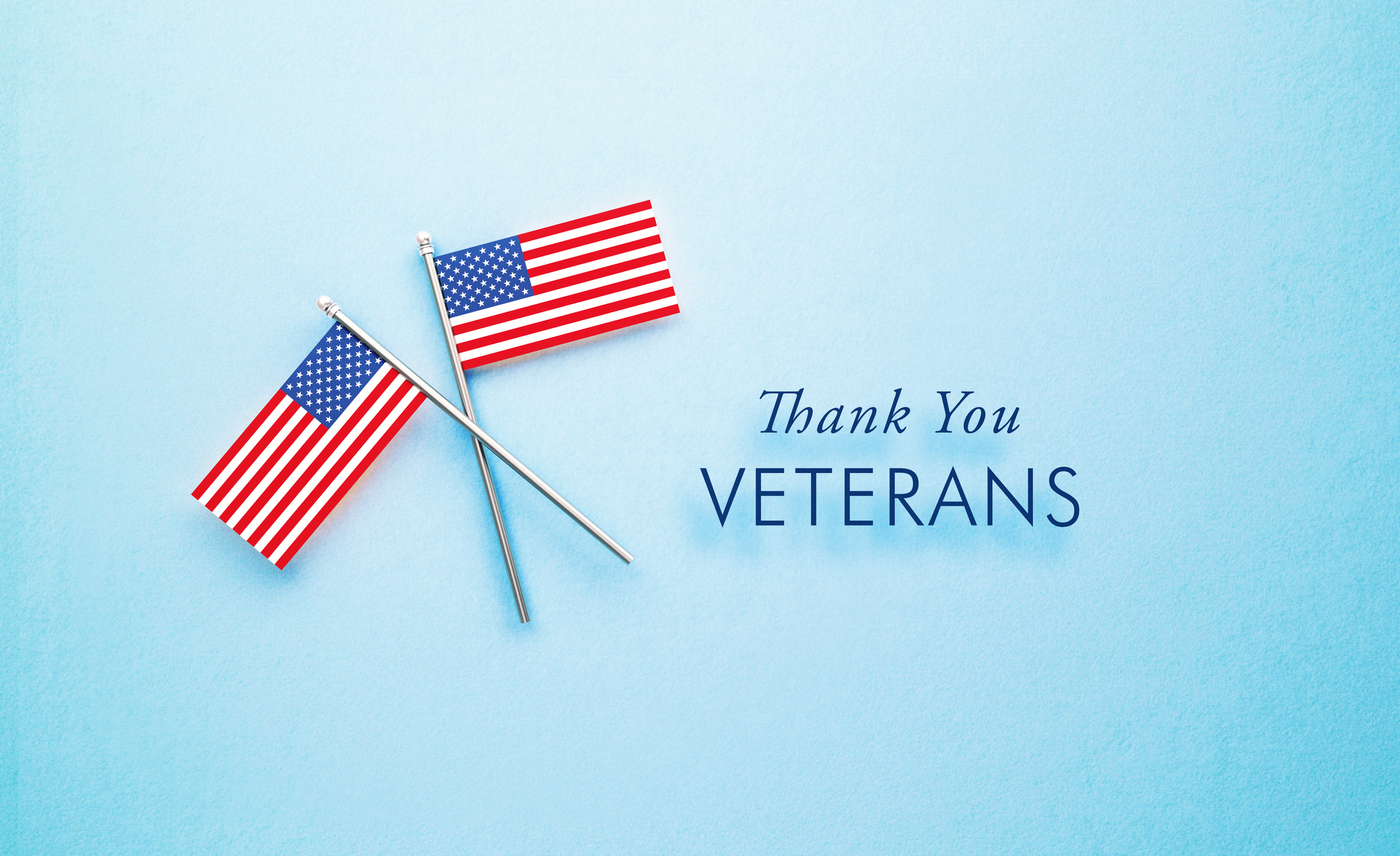 Veteran's Day Message Sitting Next To Tiny American Flag Pair On Blue Background